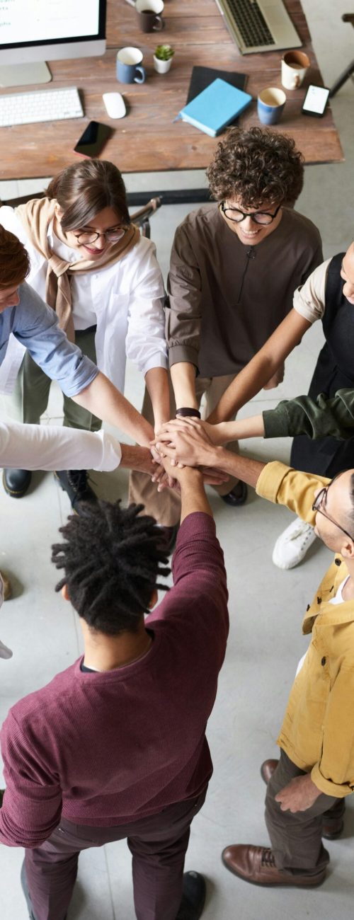 A diverse group of professionals joins hands in a team-building exercise indoors.
